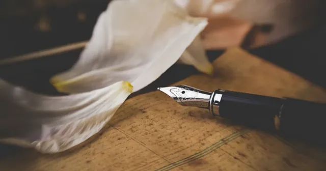 A fountain pen resting on paper, evoking a bilingual poet's craft.